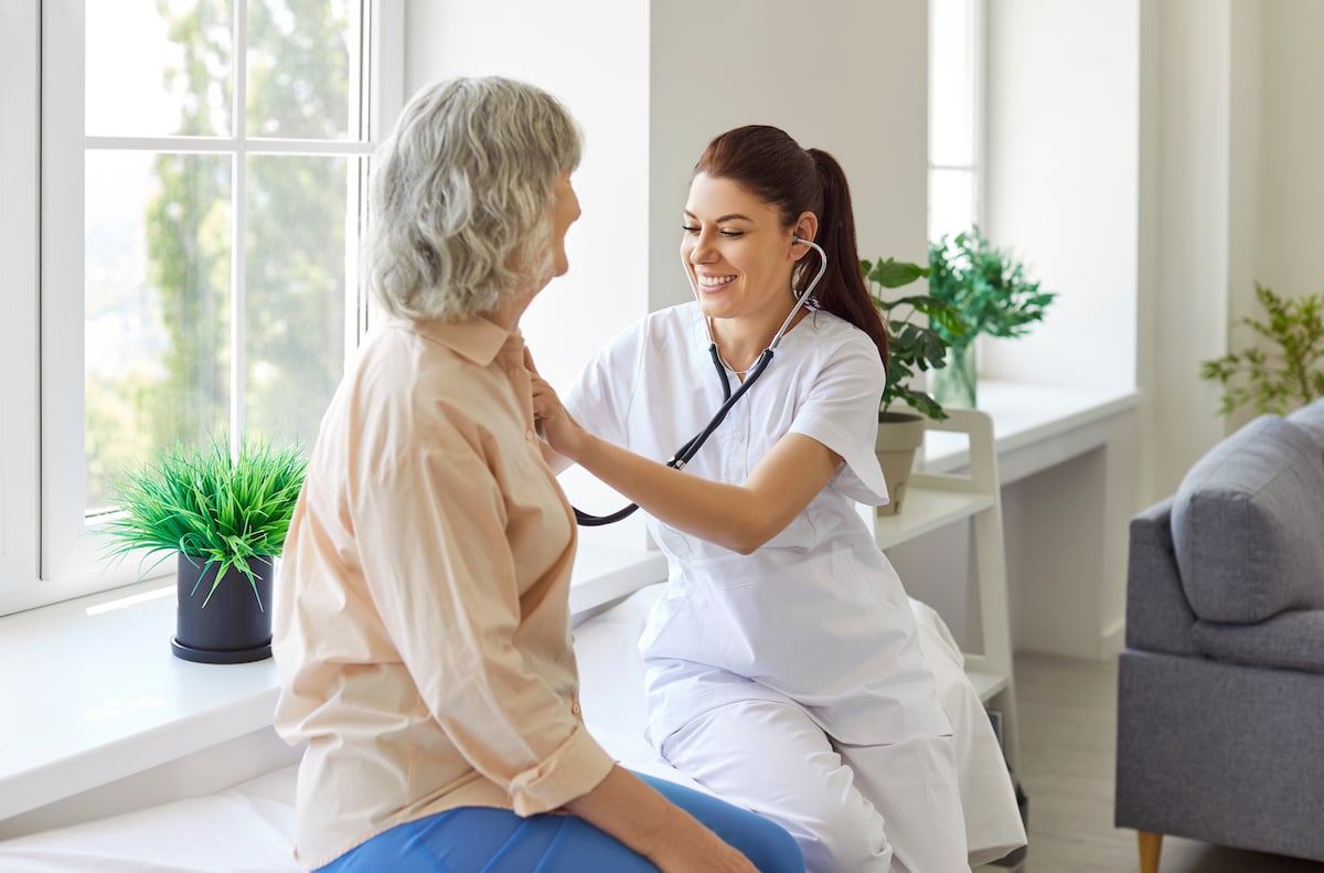 A young nurse using her stethoscope to listen to the chest of an older woman.