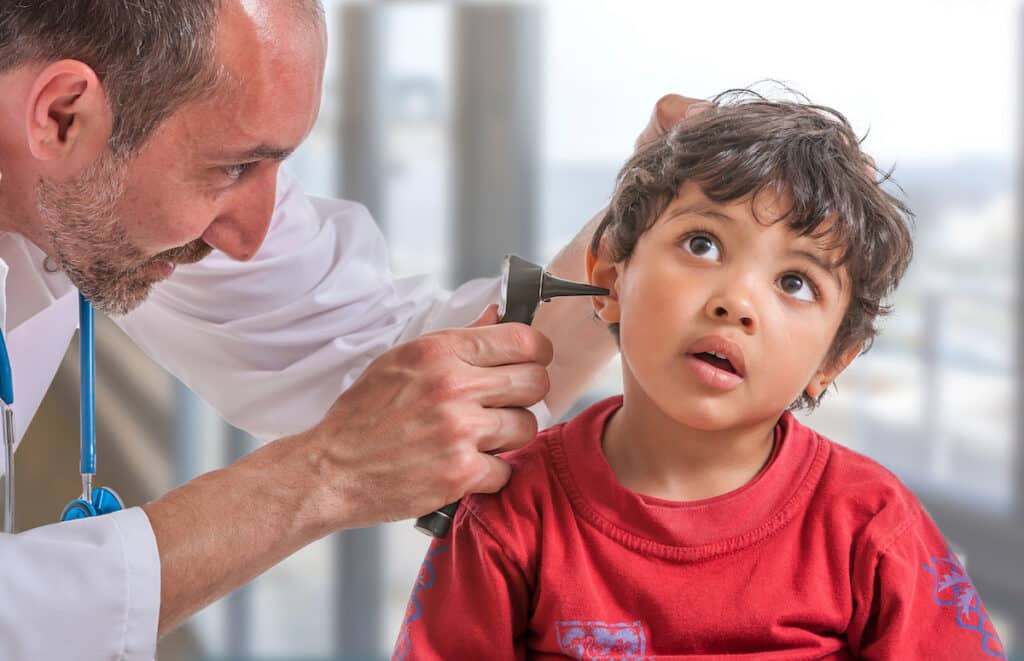 A pediatrician examines a young boy's ears during a checkup.