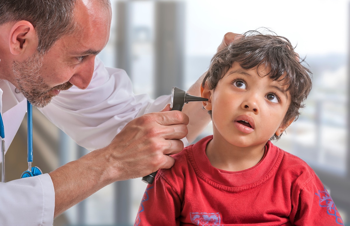 A pediatrician examines a young boy's ears during a checkup.