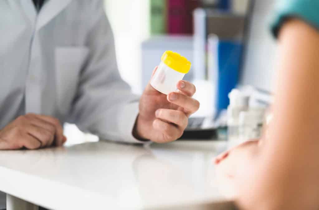 A doctor handing a drug testing cup to a patient.