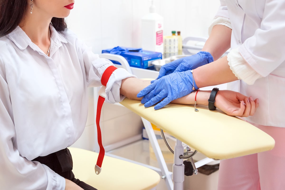 A nurse prepping a patient's arm to take blood. She has a red tourniquet around her upper arm and the doctor is cleaning the spot with gloves on.