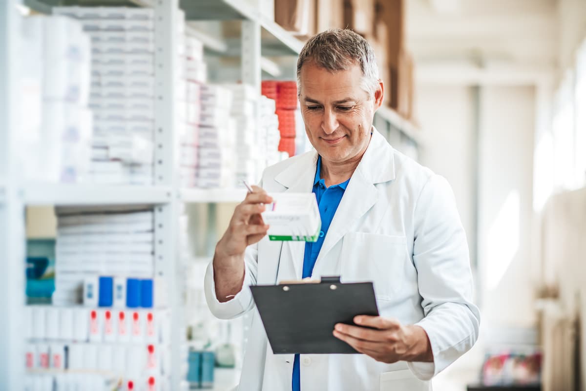 A pharmacist looking at a box of medicine and his clipboard.