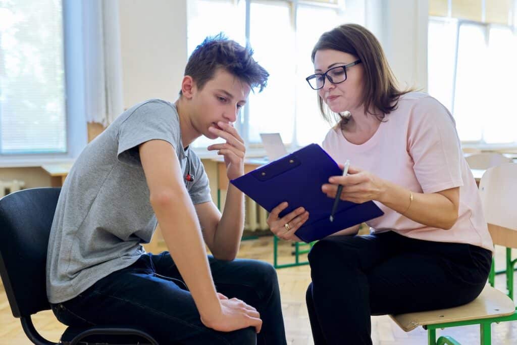 A school nurse showing a clipboard to a student sitting in a chair across from her during a school physical.