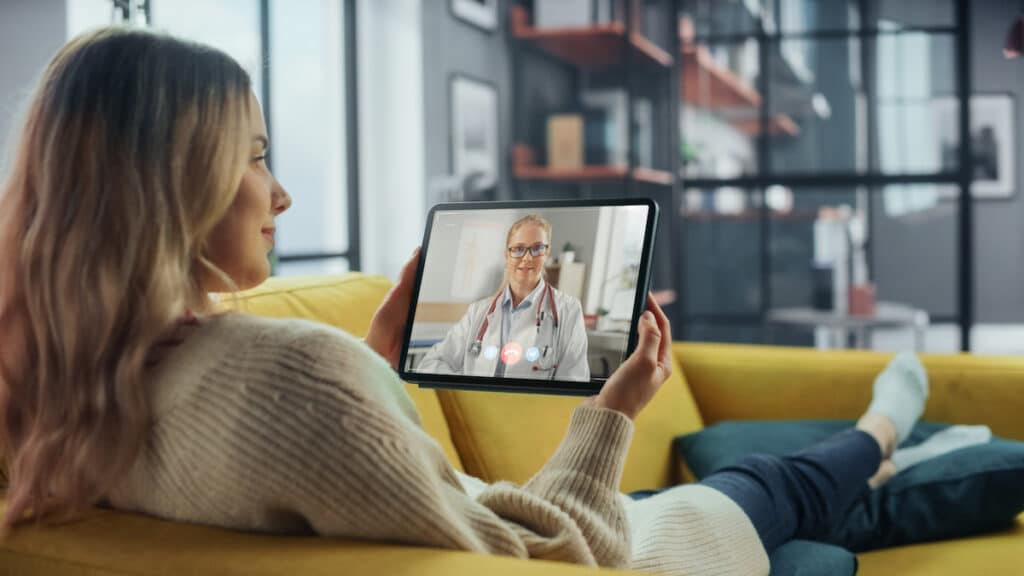 A woman having a telehealth consult with her doctor as she sits on her couch.