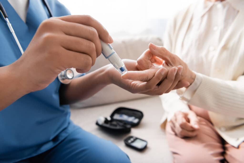 A nurse taking a blood sample from a senior woman with a lancet pen for diabetic and hypertension care.