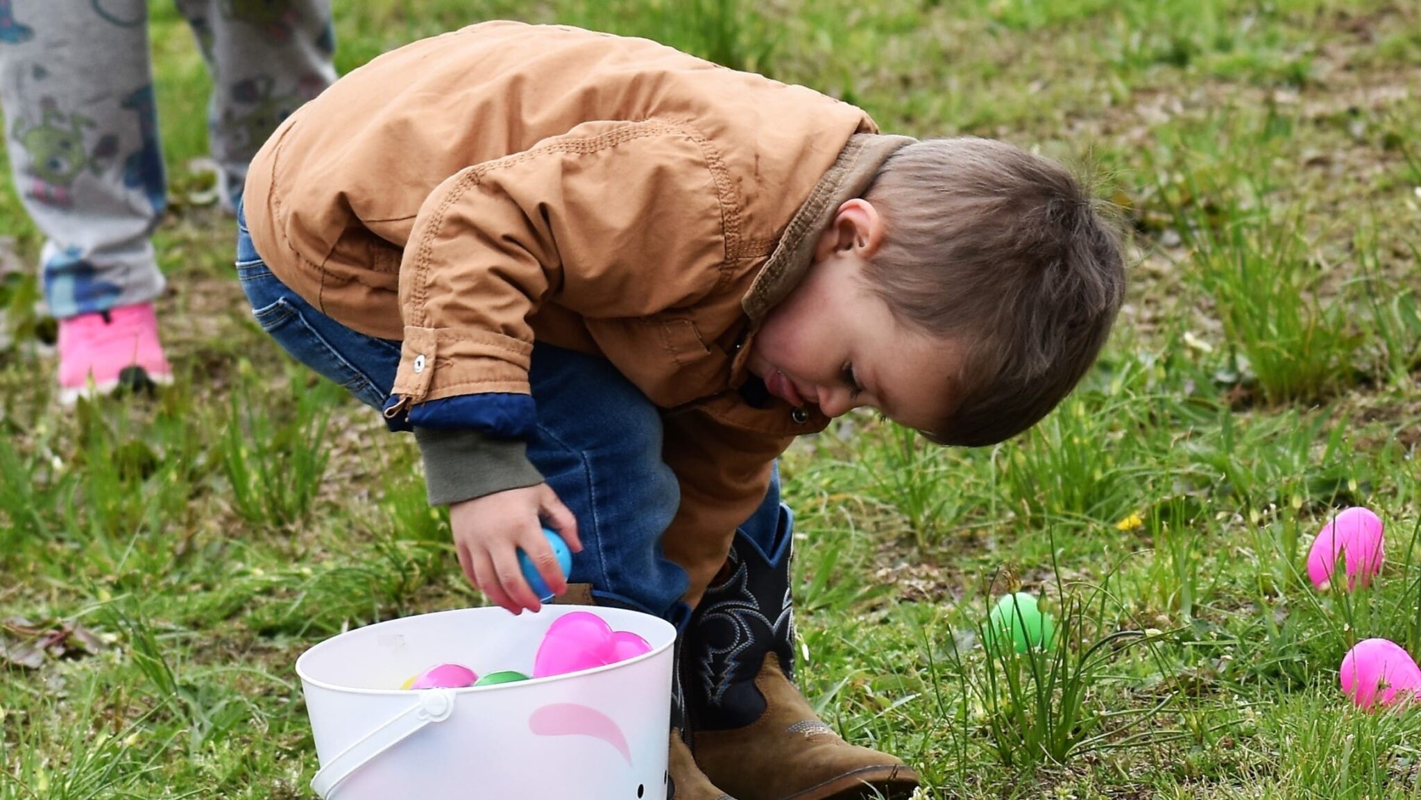 A little boy bending over to place Easter eggs in his plastic bucket.