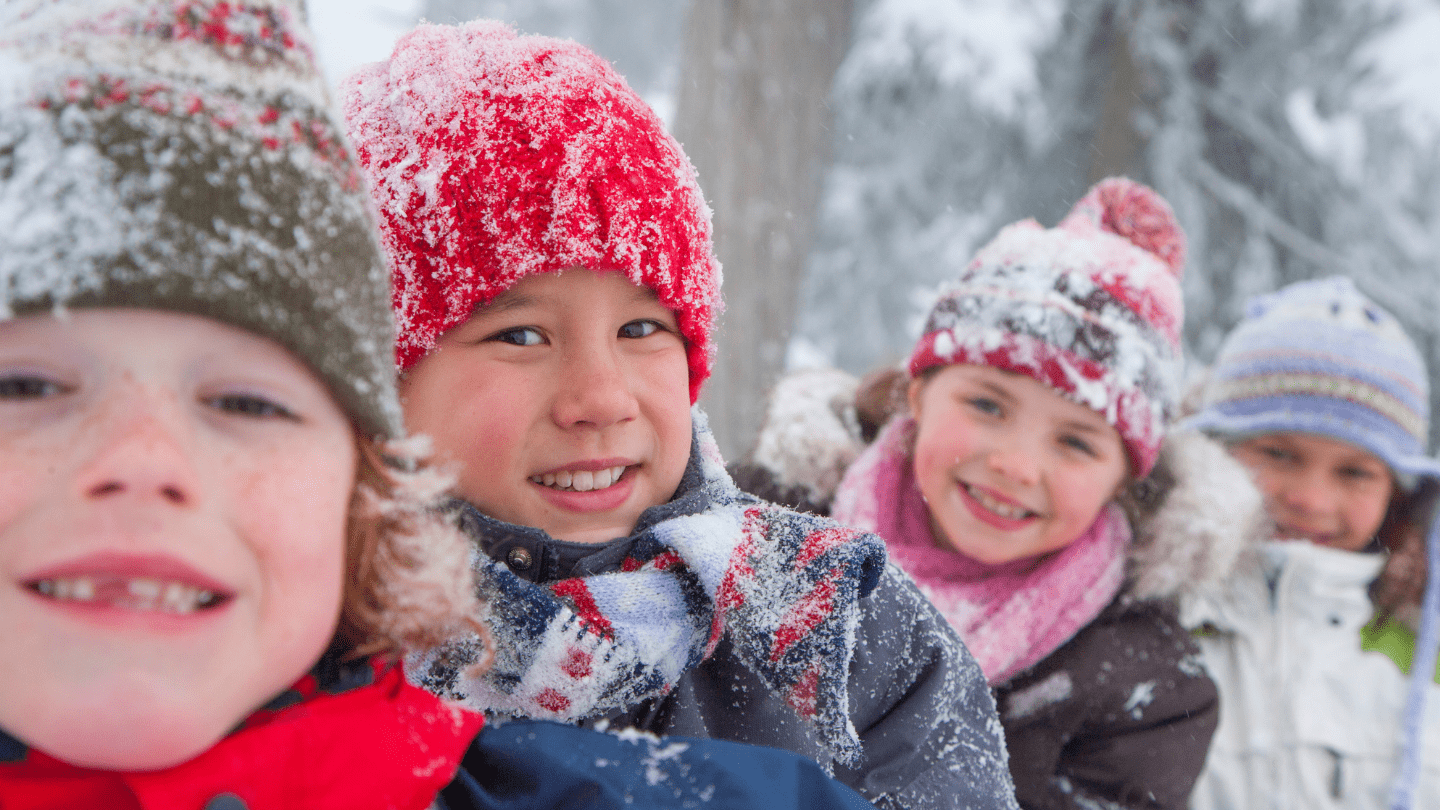 Four little kids posing for a selfie, dressed in hats, coats, and scarves and covered in snow—Explore Dr. Jeremy Porter's essential winter wellness tips for kids