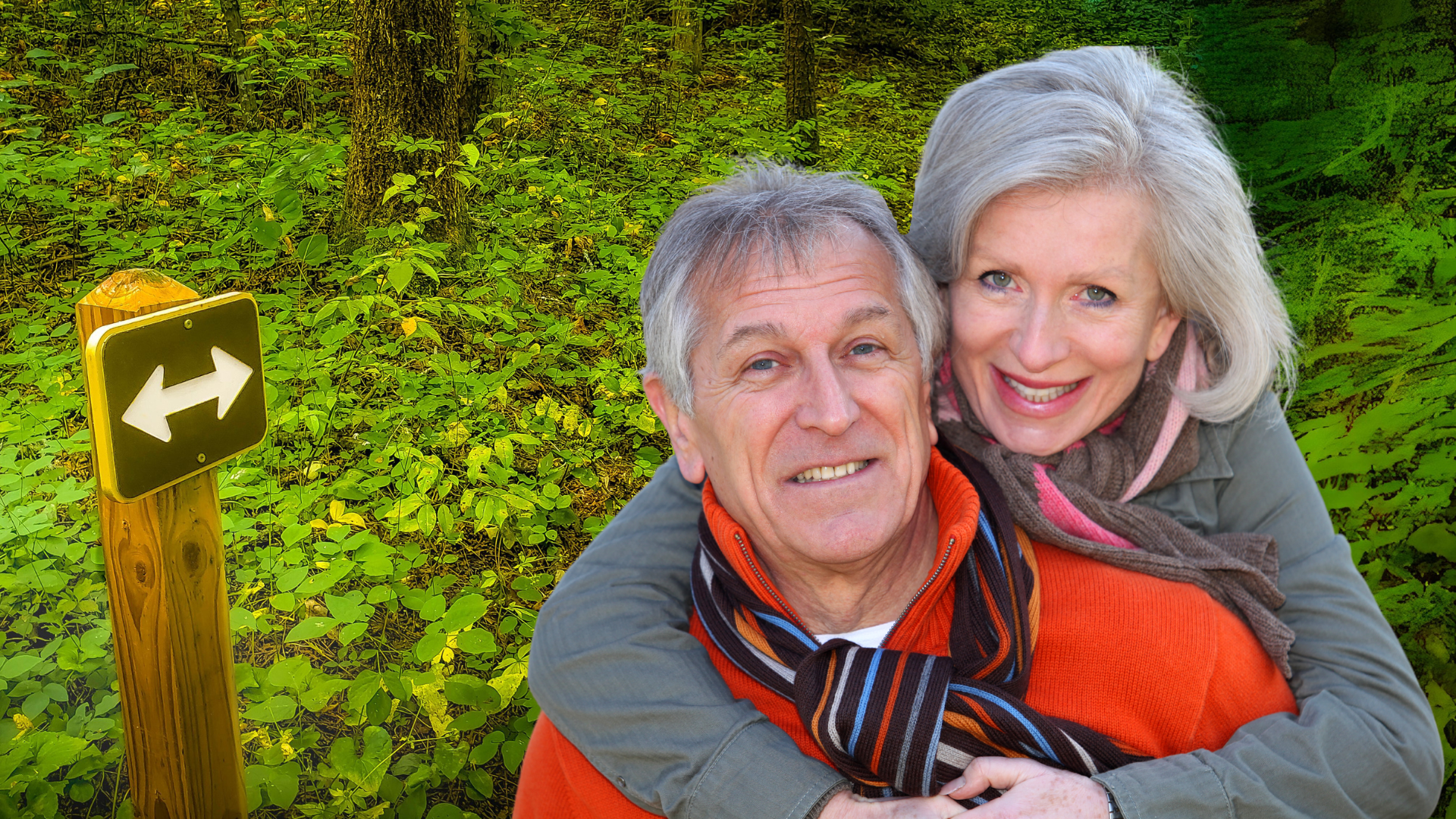 An older couple posing for a picture on a hiking trail. The woman has her hands around her husband's shoulders.
