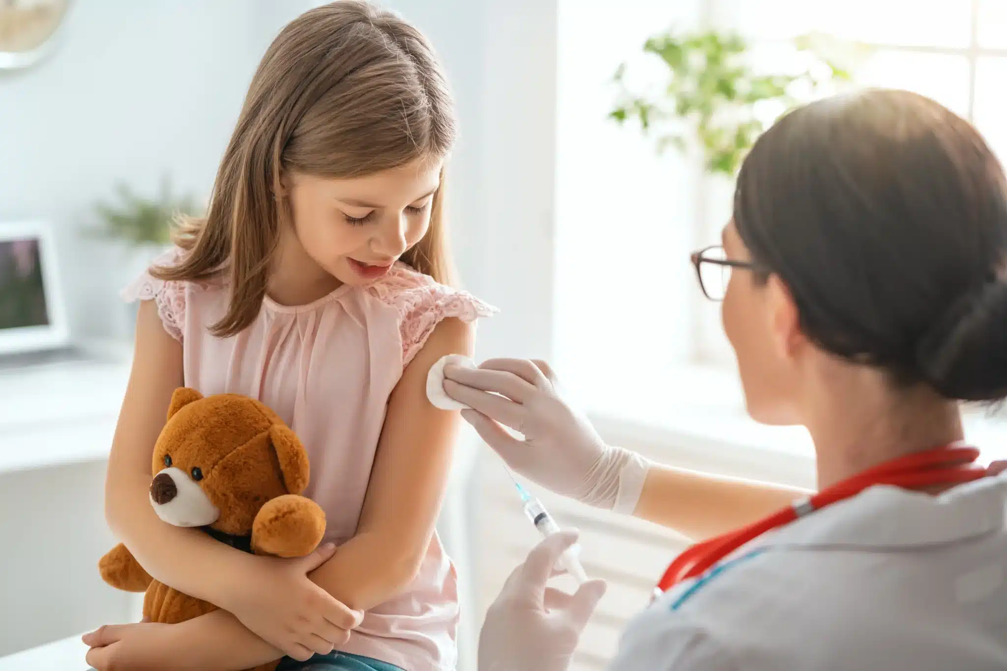 A young girl holding a teddy bear prepares for a shot. Healthy Connections offers vaccines as part of the VFC Program.
