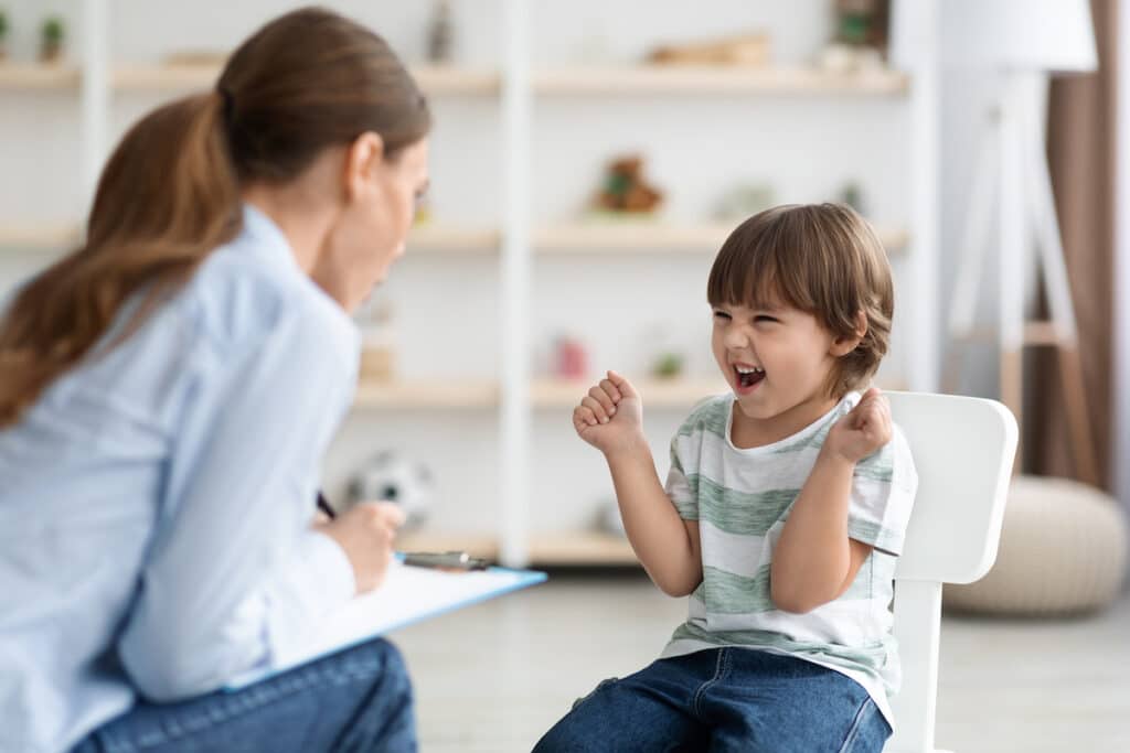 A little kid giggling and being loud and waving his hands with a child therapist for ADHD.