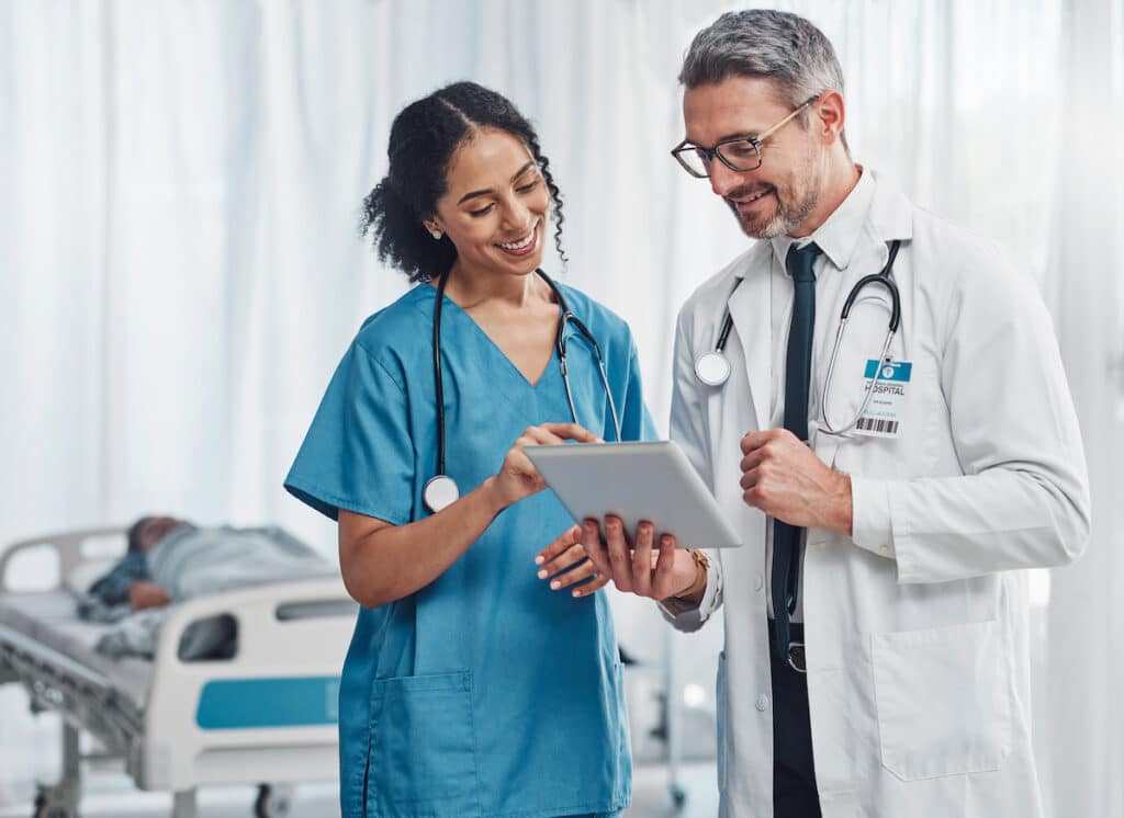 A doctor and nurse conferring and sharing notes about a patient in the room.