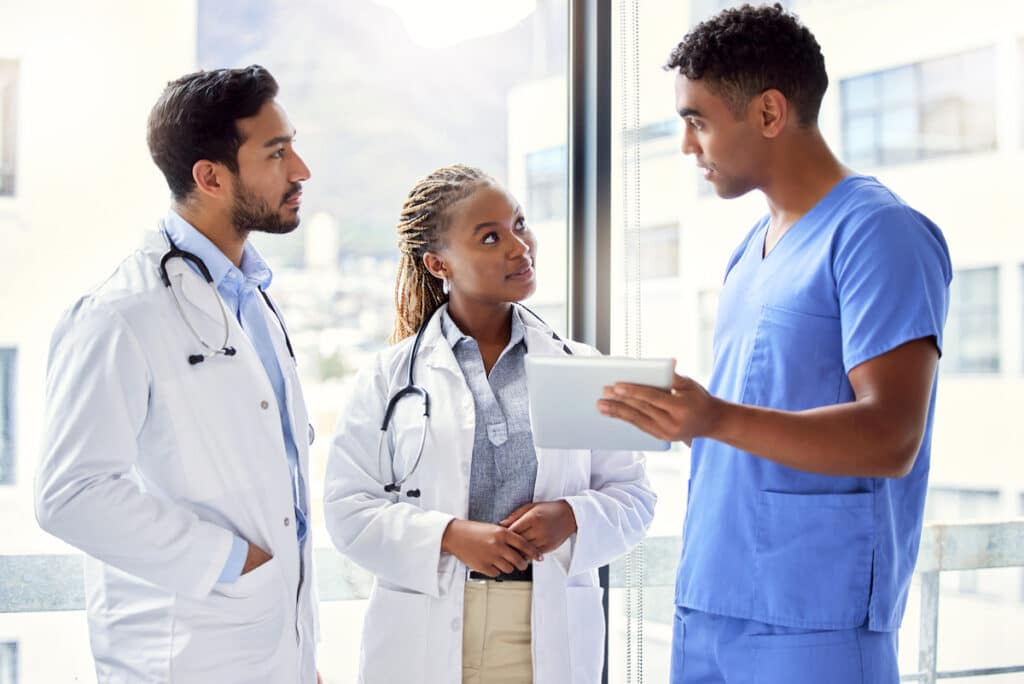 A nurse discussing results on a tablet with two doctors.