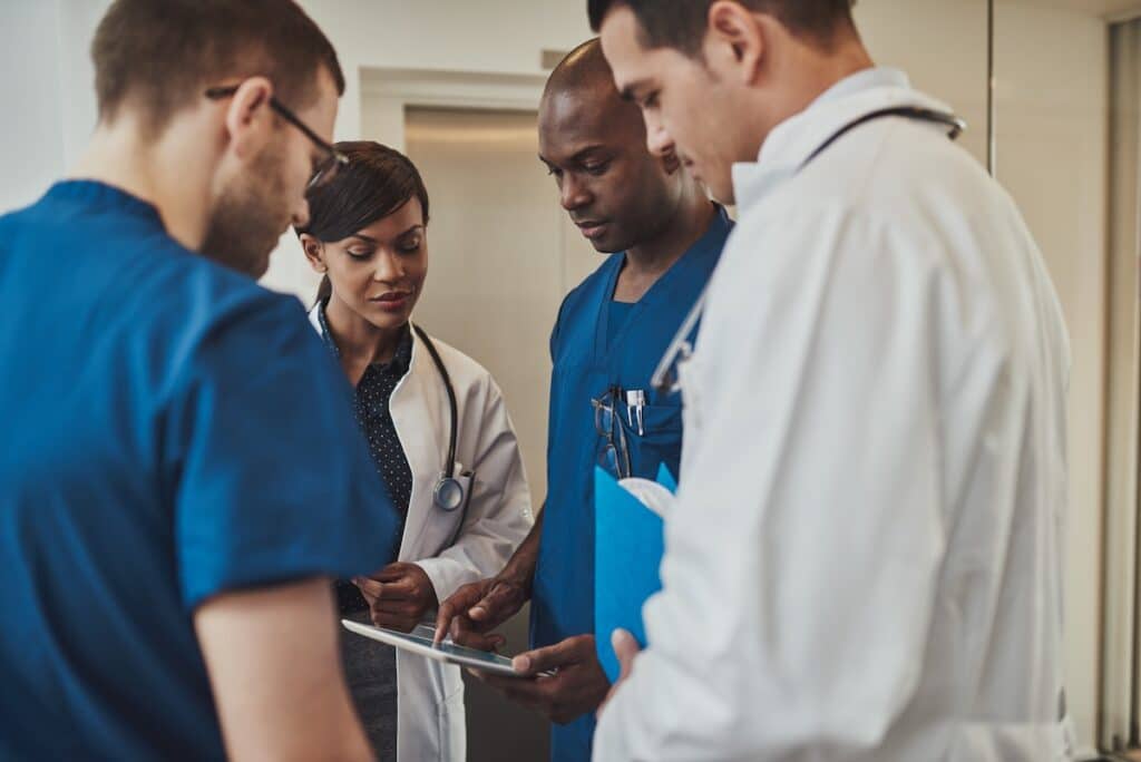 A group of multiracial doctors standing grouped closely together looking at a handheld tablet in their PCMH.