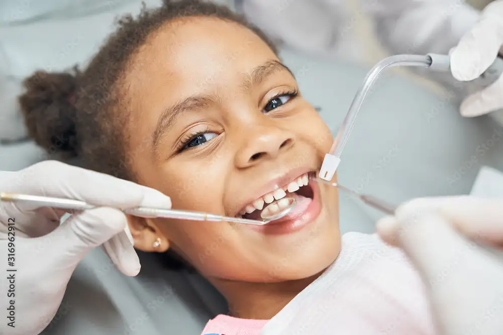 A young girl smiling with dental tools in her mouth.