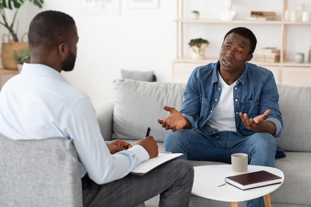 A young man sitting on a couch, talking to his counselor with Evolve Behavioral Health at Healthy Connections.