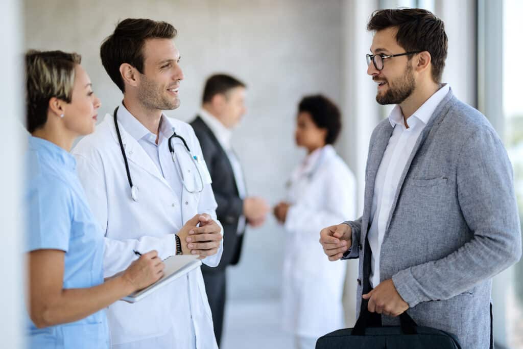 Happy doctor and nurse communicating with a businessman while standing in a hallway at medical clinic.