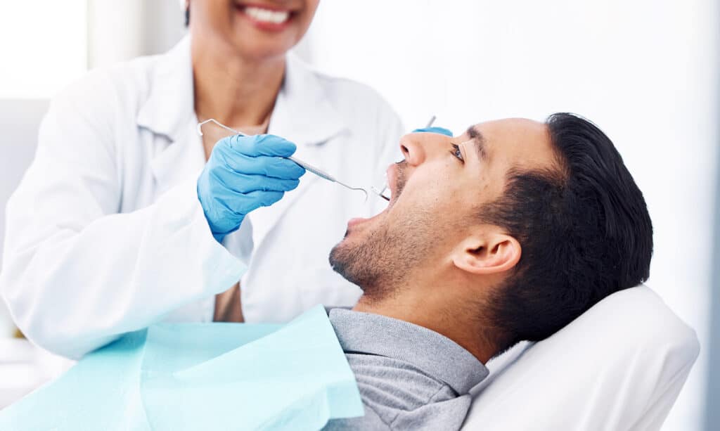 A dentist providing emergency dental care on a man's teeth as he lies in a dentist chair.