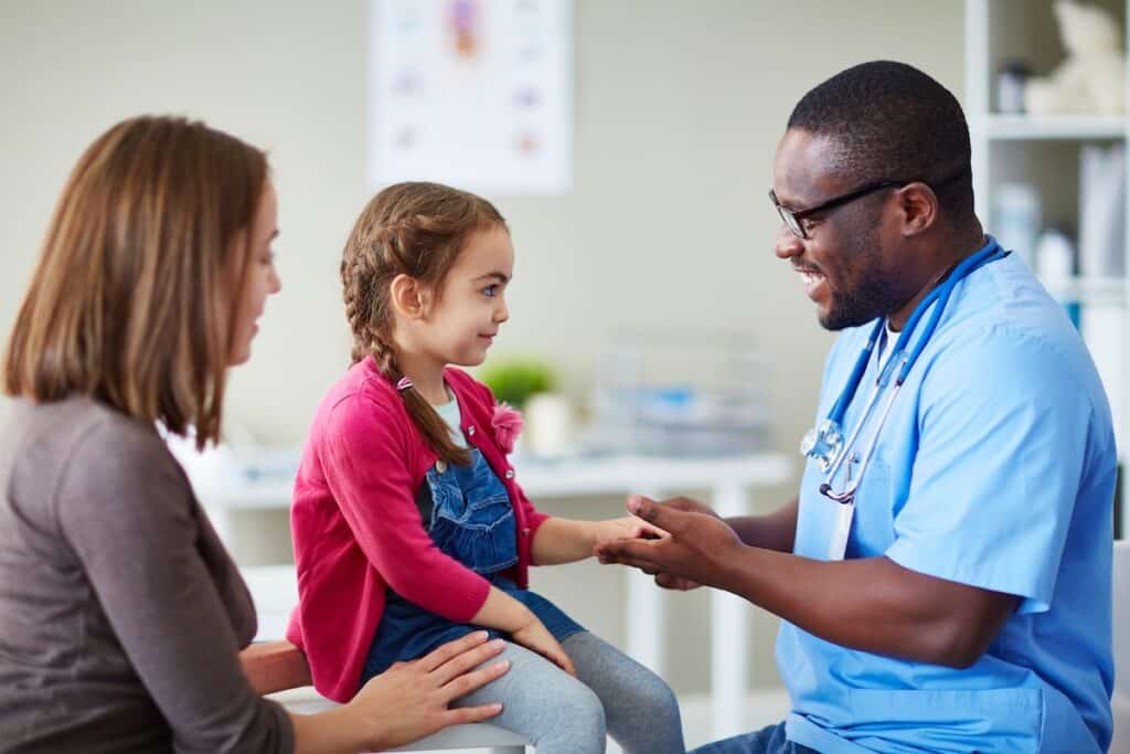 Adorable girl looking at doctor with her mother near by. Healthy Connections is a PCMH and builds strong relationships with their patients.