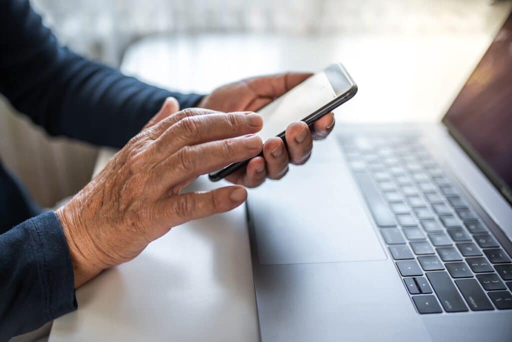 Senior person using mobile phone and laptop at home.